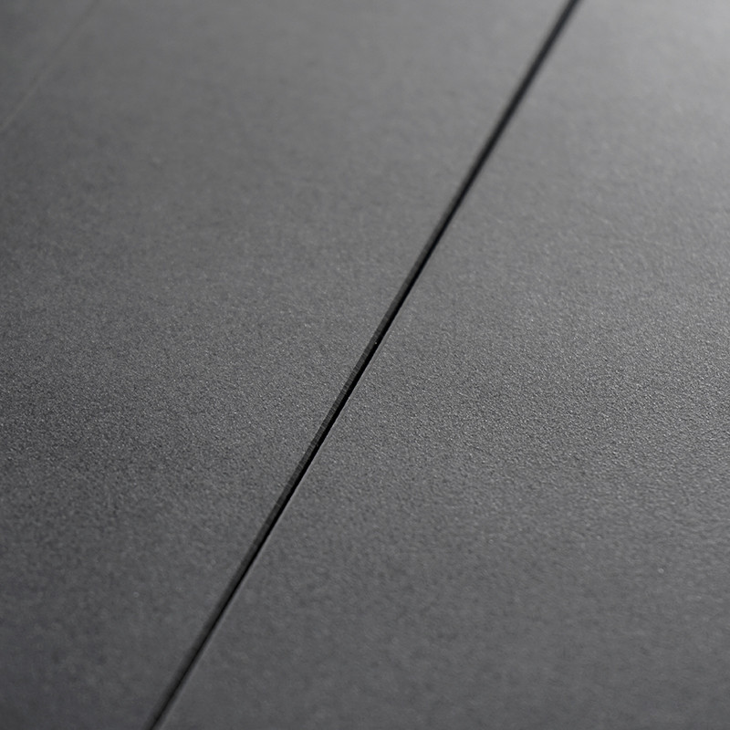 Un azulejo liso de color gris oscuro, plano, linda con otro azulejo idéntico, separado por una línea de lechada estrecha y recta