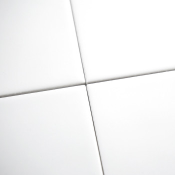 Vier gladde, witte keramische tegels vormen een netjes raster dat elkaar op de hoeken kruist, waardoor een symmetrisch patroon o