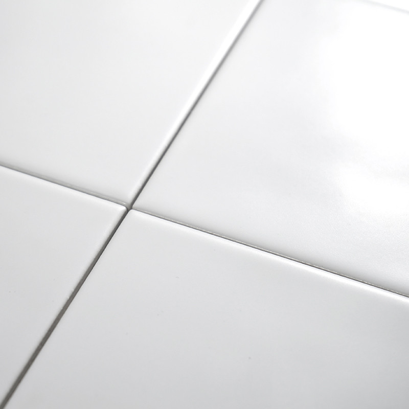 Four glossy white ceramic tiles intersect, forming a grid pattern on a smooth surface, reflecting light in a bright setting.