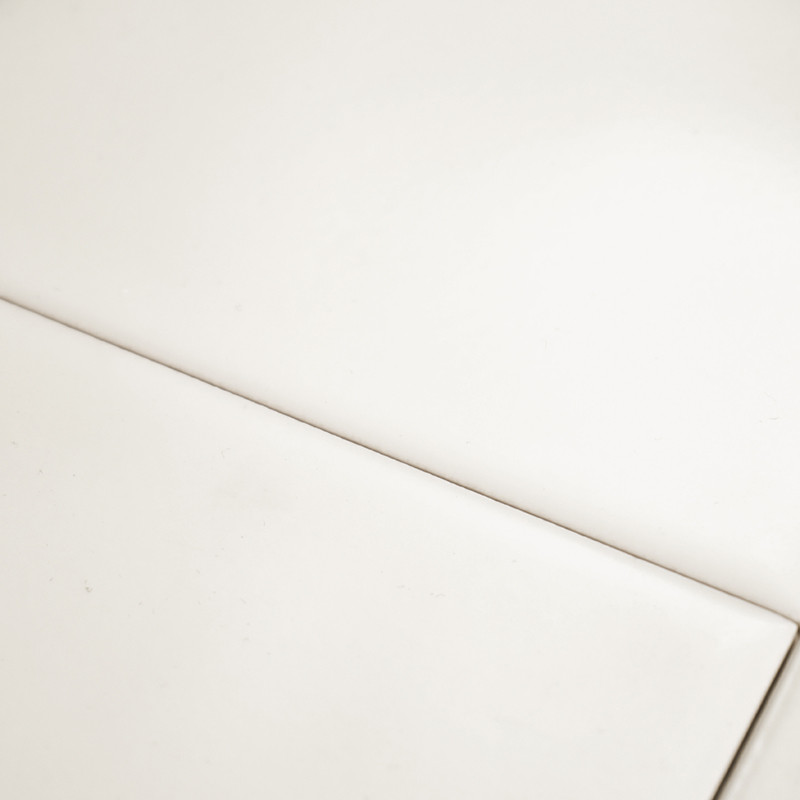 Un azulejo blanco liso y brillante yace plano, cruzado por una línea de lechada delgada y recta, creando un patrón geométrico mi