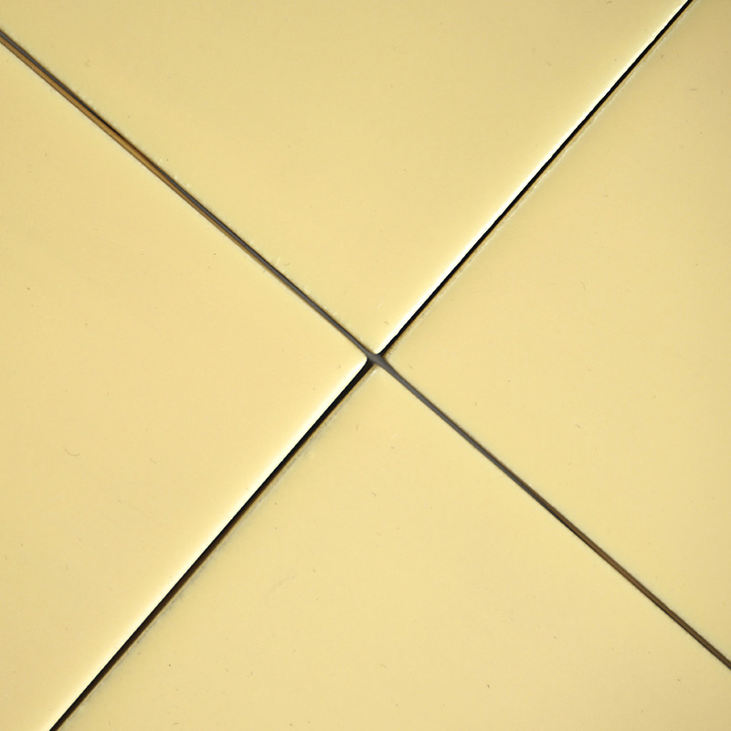 Quatre carreaux lisses, carrés et jaune pâle se rejoignent au centre, formant un motif croisé symétrique. chaque carreau est sép