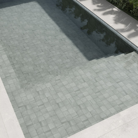 Hellgraue Steinfliesen bilden einen unter Wasser liegenden Poolboden, der das Sonnenlicht reflektiert und von Betonrändern und g Hellgraue Steinfliesen bilden einen unter Wasser liegenden Poolboden, der das Sonnenlicht reflektiert und von Betonrändern und g
