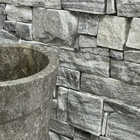 Stone tiles form a textured wall behind a cylindrical stone basin, creating a rustic, natural setting.