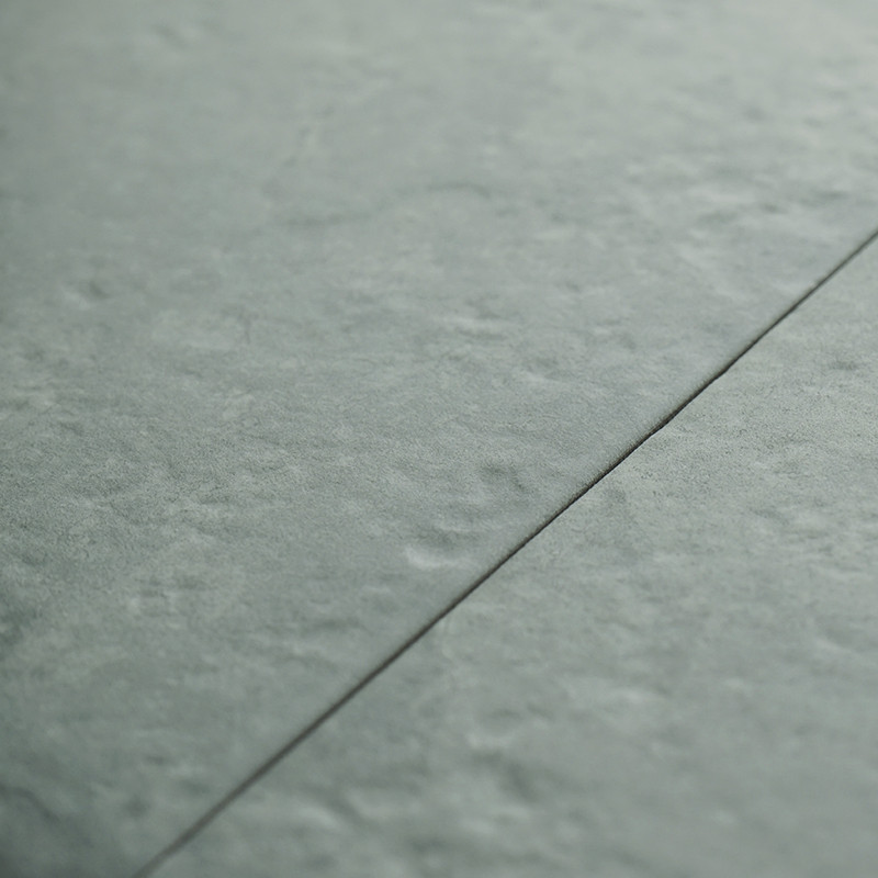A lightly textured, gray-green tile is joined by a fine, dark grout line, laid in a seamless indoor floor pattern.
