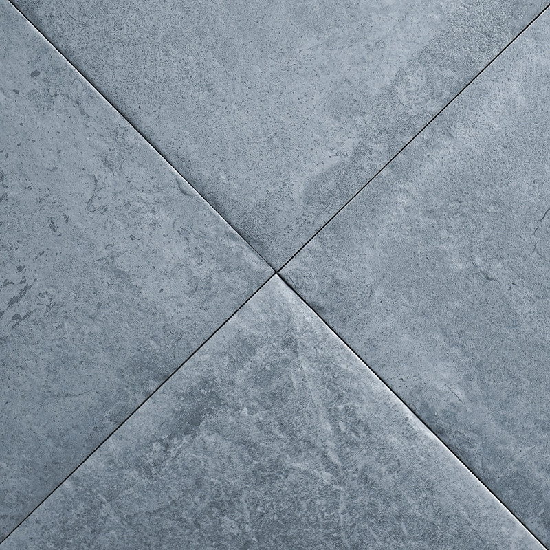 Cuatro azulejos de color gris oscuro forman un patrón en X con un sutil veteado, creando una superficie texturizada en un ambien
