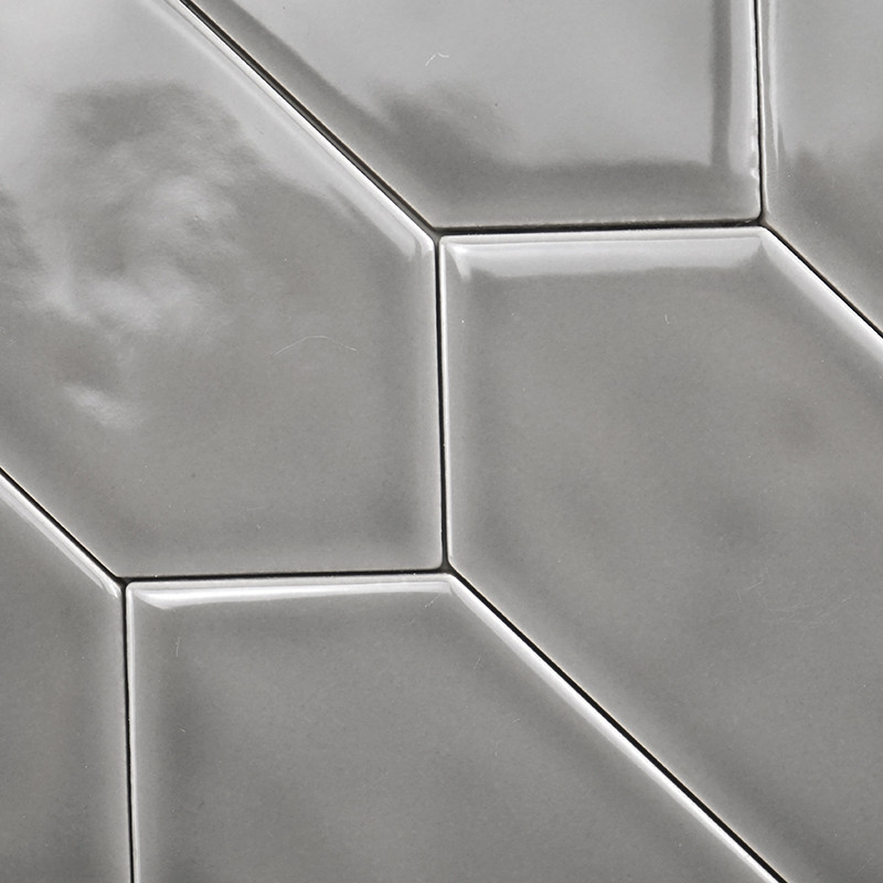 Les carreaux de céramique gris brillants forment un motif géométrique avec des bords surélevés et inclinés, créant une texture é
