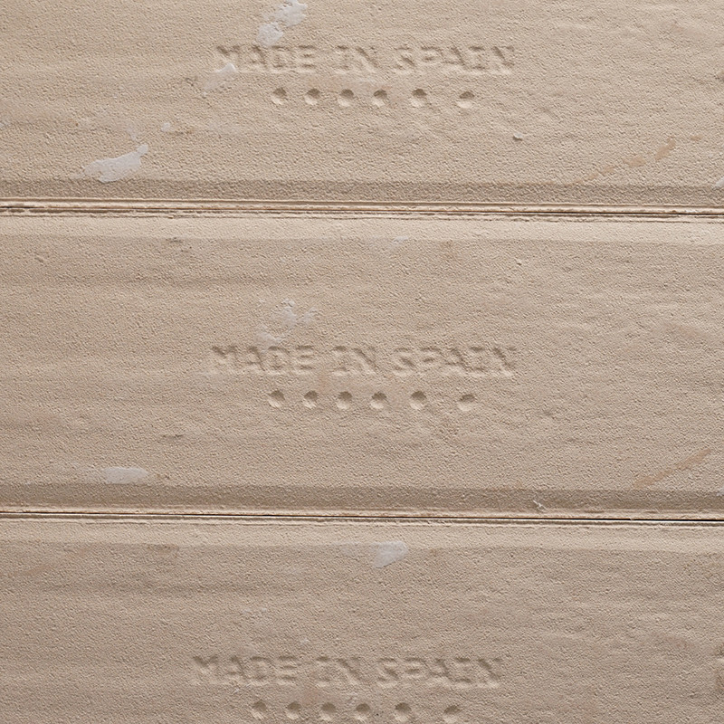 De tekst in reliëf `MADE IN SPAIN` verschijnt op beige tegelranden, met kleine stippen onder elke zin, die de oorsprong van de p