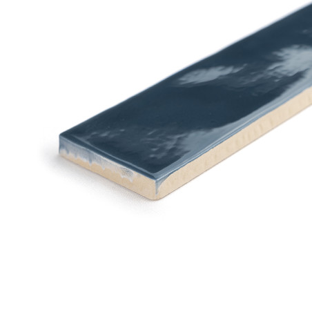 Un carreau de céramique rectangulaire présente une surface bleu foncé brillante avec un bord beige, posée à plat sur un fond bla