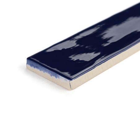 Un azulejo cerámico rectangular muestra un esmalte azul oscuro brillante en la parte superior, con bordes sin vidriar que revela Un azulejo cerámico rectangular muestra un esmalte azul oscuro brillante en la parte superior, con bordes sin vidriar que revela