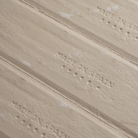 Auf der hellbraunen Kachel ist der Text „MADE IN SPAIN“ eingeprägt, gefolgt von vier Punkten, die in parallelen Linien angeordne