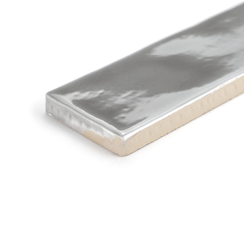 A rectangular ceramic tile displays a glossy silver metallic finish, resting on a plain white surface. Its reflective surface ex