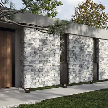 Stone wall tiles cover the exterior of a modern building, surrounded by a concrete pathway and green lawn.
