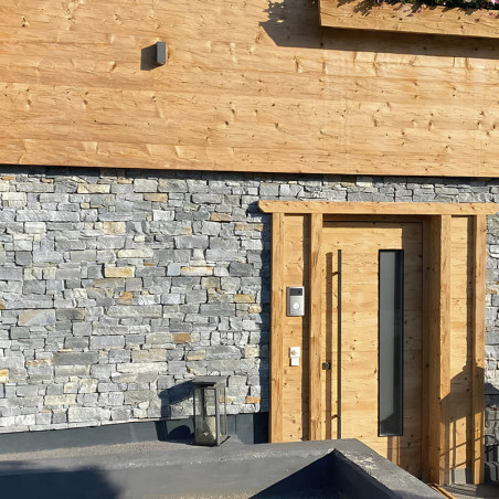 Stenen tegels creëren een gestructureerde muur naast een houten deur in een moderne woonentree. Stenen tegels creëren een gestructureerde muur naast een houten deur in een moderne woonentree.