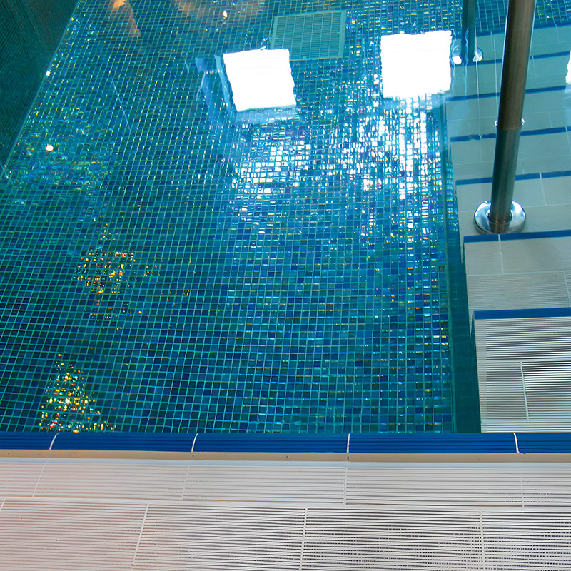Uma piscina de mosaico de vidro reflete a luz solar, criando padrões brilhantes em uma piscina coberta com grades de metal visív