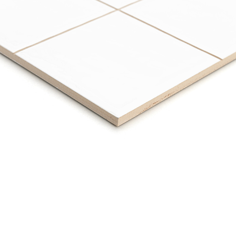 Un carreau de céramique blanche divisé en quatre carrés repose sur un fond uni, montrant sa surface lisse et ses bords nets et d
