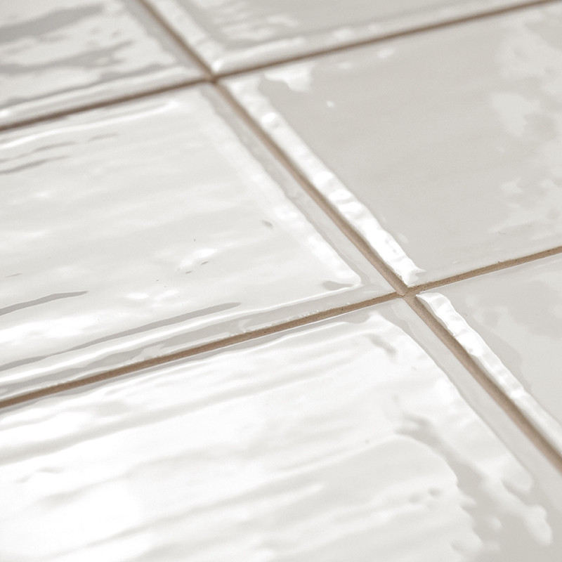 Les carreaux de céramique blanche présentent une surface brillante avec des textures légèrement ondulées, disposées selon un mot