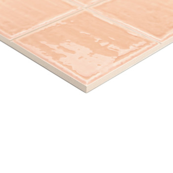 Een keramische tegel met een glanzende, perzikkleurige afwerking vertoont een rasterpatroon, rustend op een wit oppervlak, wat e