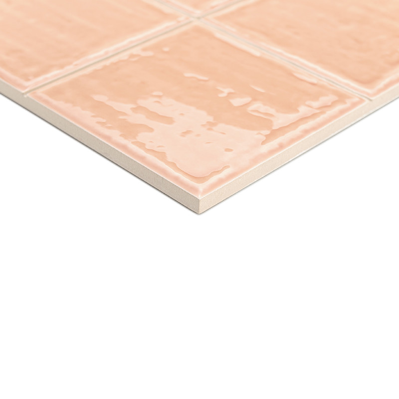 Un carreau de céramique au fini brillant de couleur pêche affiche un motif quadrillé, posé sur une surface blanche, suggérant un