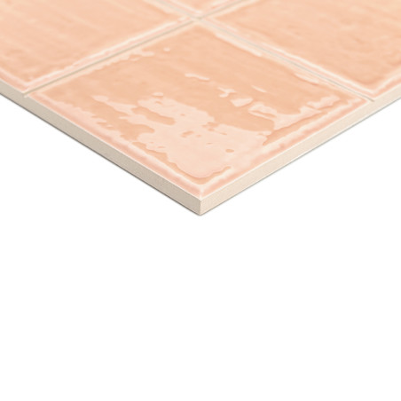 Een keramische tegel met een glanzende, perzikkleurige afwerking vertoont een rasterpatroon, rustend op een wit oppervlak, wat e