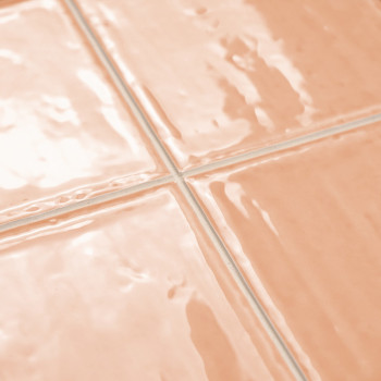 Vier glanzende, perzikkleurige keramische tegels in een netjes raster reflecteren het licht. De voeg daartussen vormt strakke, w