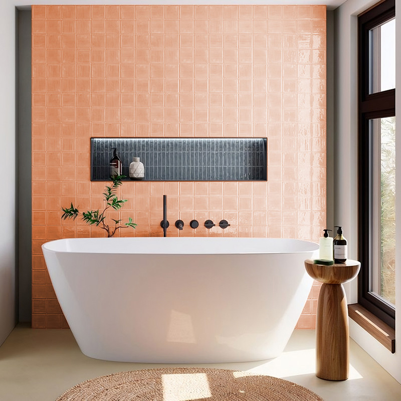 Uma banheira independente branca repousa contra uma parede de azulejos cor de pêssego com uma prateleira preta embutida com deco