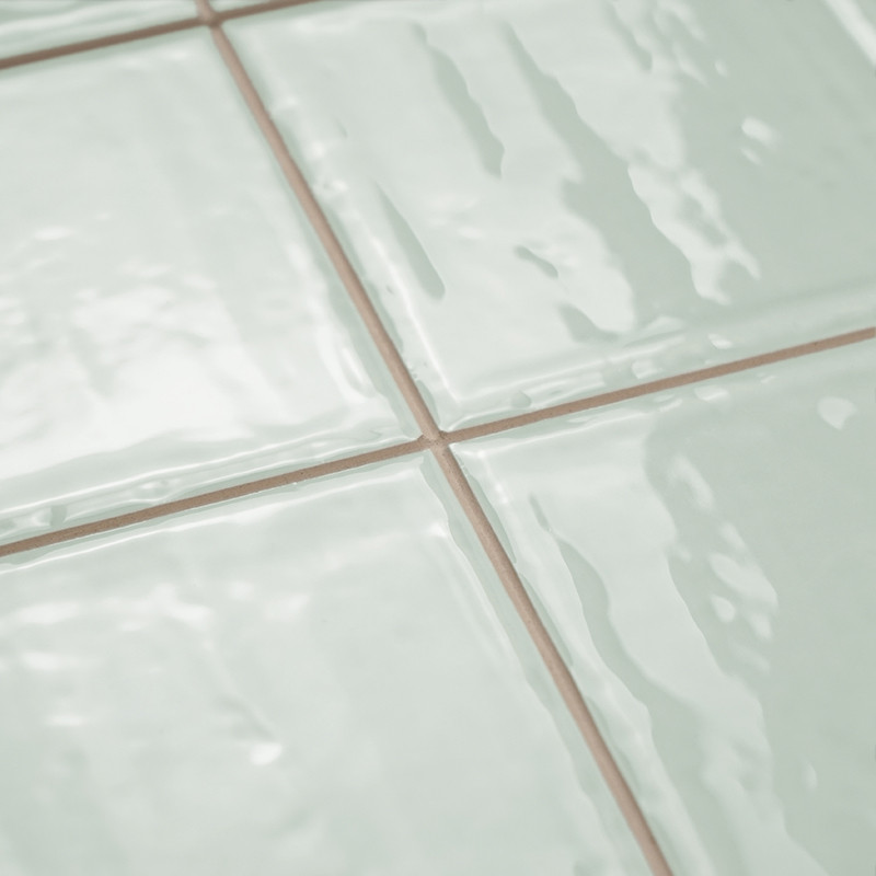 Quatro ladrilhos cerâmicos verdes claros e brilhantes estão dispostos em um padrão de grade. A superfície lisa reflete a luz, cr