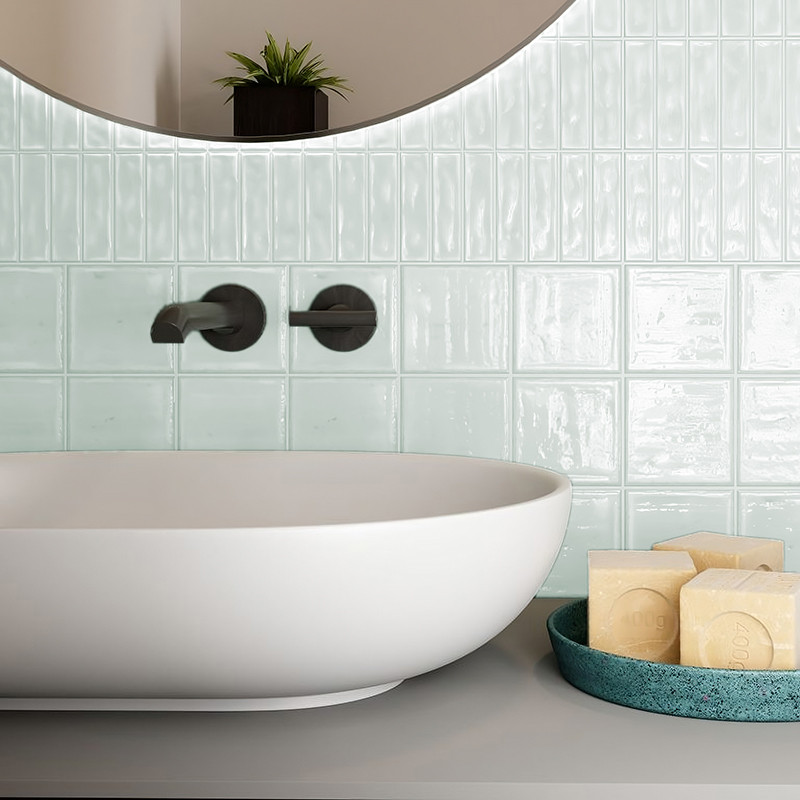 Uma pia de cerâmica branca repousa contra uma parede de azulejos verde-claros brilhantes, acompanhada por uma travessa azul-petr