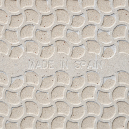 Tile features embossed, overlapping semicircular pattern. `MADE IN SPAIN` inscribed in center. Background is a light beige color
