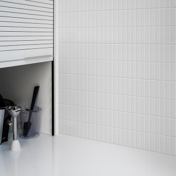 Los azulejos verticales blancos del metro cubren una pared y reflejan la luz en una cocina elegante y moderna con gabinetes y un