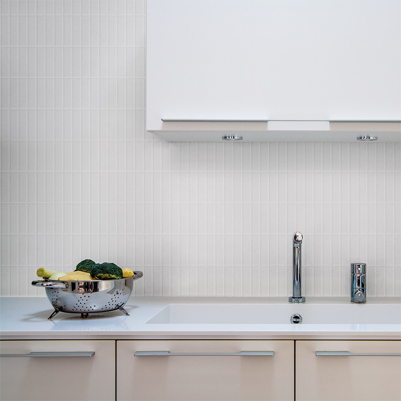 Uma peneira de metal com vegetais fica em uma bancada branca perto de uma pia moderna com torneira cromada, contra um backsplash