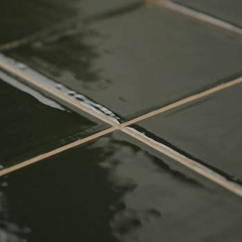 Glossy green ceramic tiles form a gridded pattern, reflecting light. They are neatly aligned, creating a smooth, shiny surface i