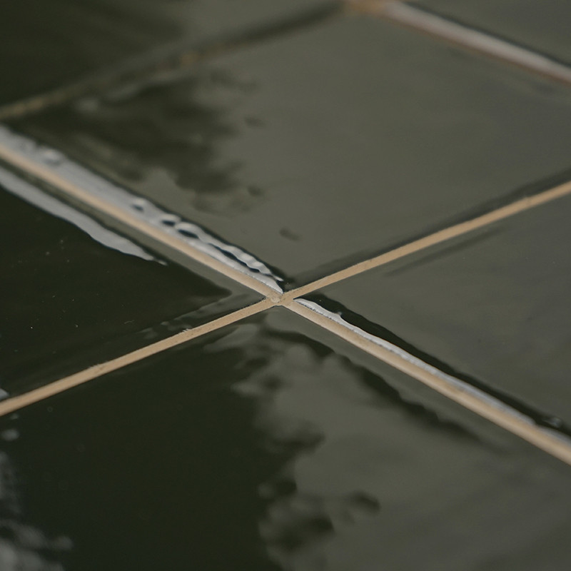 Ladrilhos cerâmicos verdes brilhantes formam um padrão de grade, refletindo a luz. Eles estão perfeitamente alinhados, criando u
