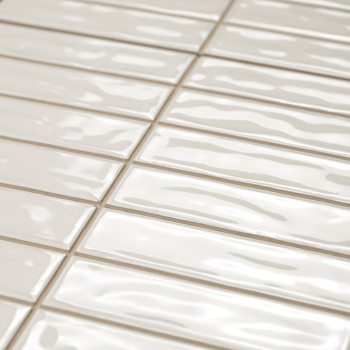 Rechthoekige, glanzende beige tegels zijn in een verspringend patroon gerangschikt. Het oppervlak heeft golvende texturen, die l