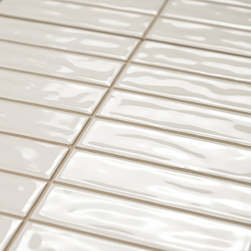 Rectangular, glossy beige tiles are arranged in a staggered pattern. The surface has wavy textures, reflecting light in a smooth