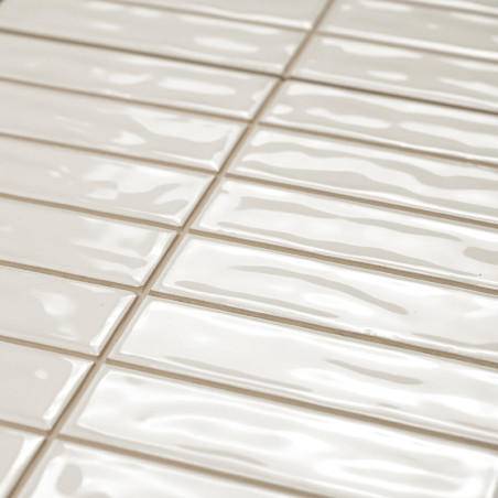 Rechthoekige, glanzende beige tegels zijn in een verspringend patroon gerangschikt. Het oppervlak heeft golvende texturen, die l