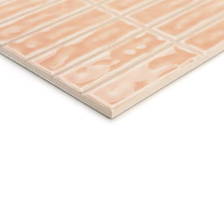 Een rechthoekige, perzikkleurige keramische tegel heeft een glanzend, golvend oppervlaktepatroon. Het is gerangschikt in een ras