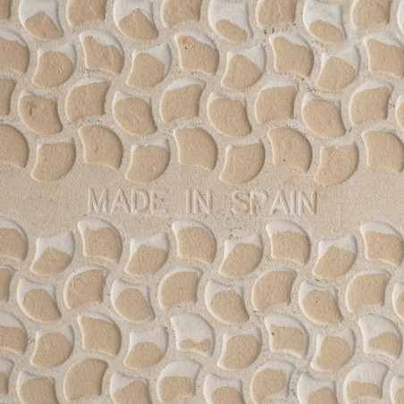 De tegel heeft een patroon van verhoogde, gebogen beige vormen met lichte voeglijnen, met in het midden de tekst `MADE IN SPAIN`