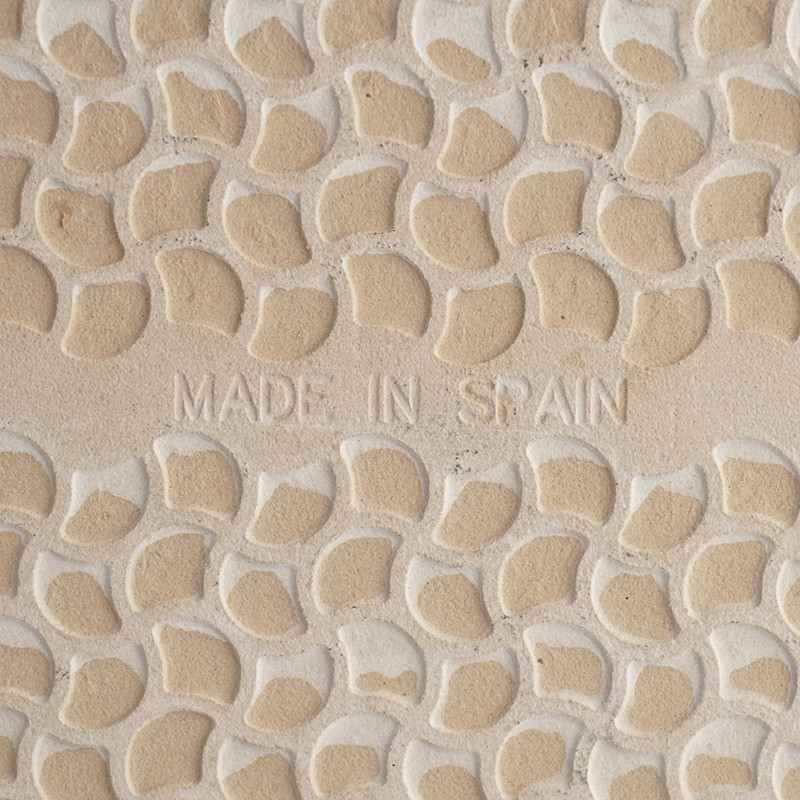 Embossed ceramic tile featuring small, crescent-shaped raised patterns. The words `MADE IN SPAIN` are centrally inscribed, enhan