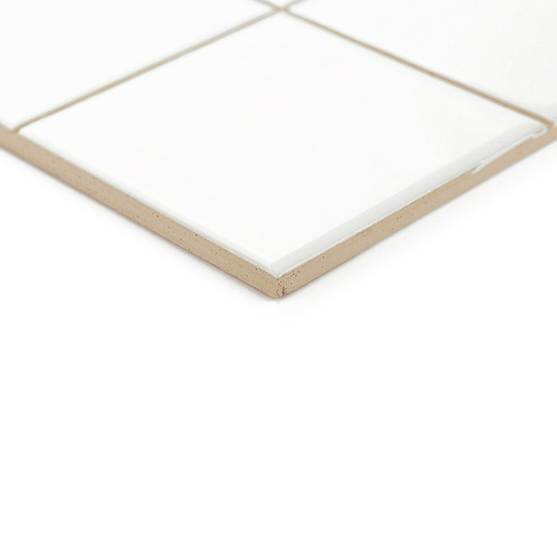 A ceramic tile with a glossy white surface sits on a beige base, forming part of a grid in a minimalist setting.