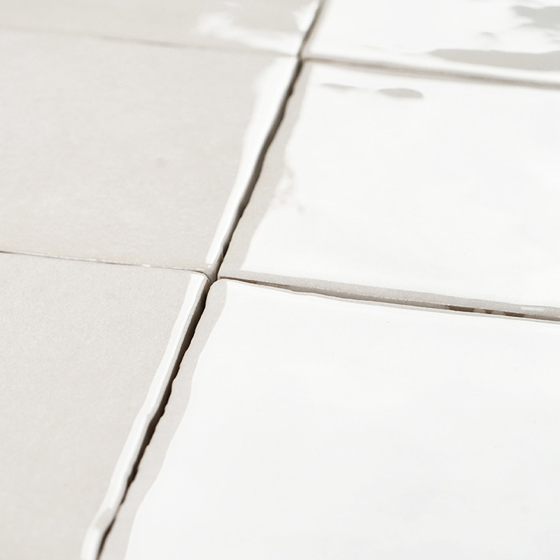 Les carreaux carrés blancs aux surfaces réfléchissantes sont plats, alignés selon un motif en grille. Le coulis entre eux est lé