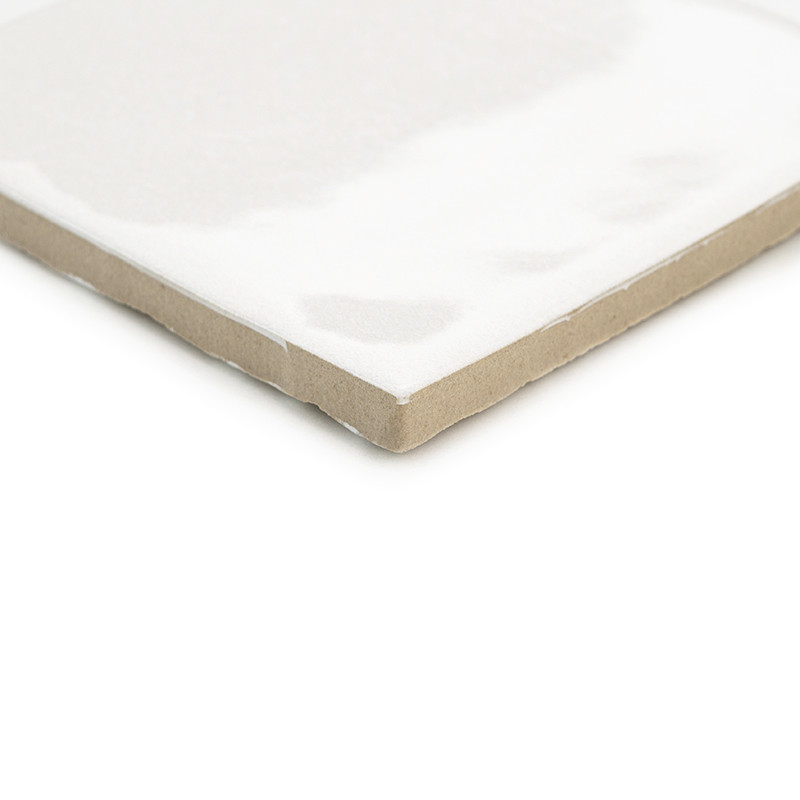 Eine weiße Keramikfliese mit glänzender Oberfläche liegt schräg und weist eine beige, unglasierte Kante auf, was ein klares, min