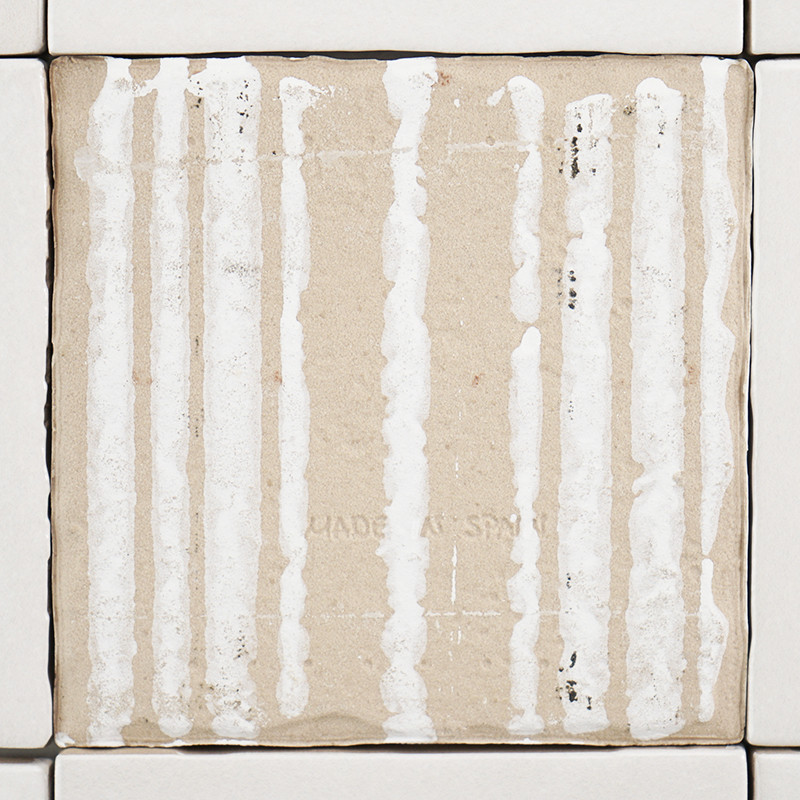 Un carreau de céramique beige, comportant des stries blanches verticales, est placé au centre parmi des carreaux blancs plus pet