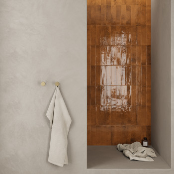 Eine glänzende, rotbraun geflieste Wand bildet einen Duschbereich mit einem Handtuch, das über einen Haken an einer glatten, hel