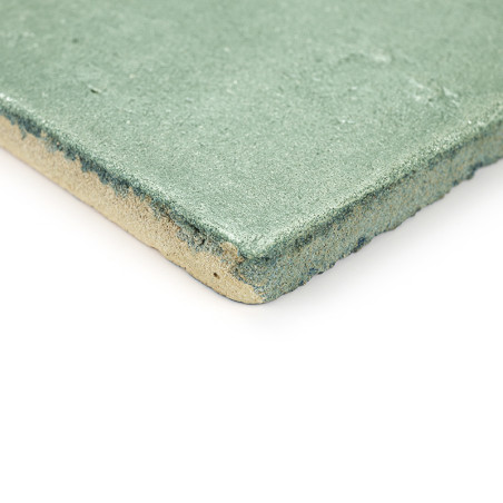 Los azulejos de terracota verde se encuentran en ángulo, mostrando una textura rugosa y bordes en capas sobre un fondo blanco li