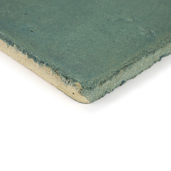 Un azulejo de terracota cuadrado, texturizado, verde azulado yace plano, mostrando bordes ásperos visibles sobre un fondo blanco