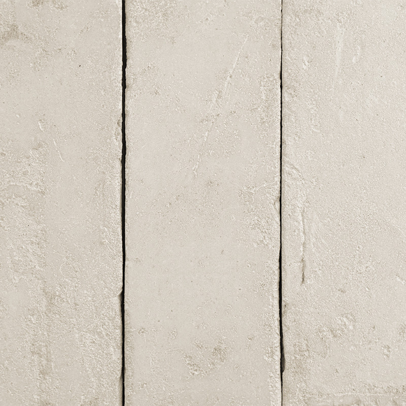 Des carreaux rectangulaires en terre cuite sont alignés, présentant une texture rugueuse et une couleur beige clair, créant une 