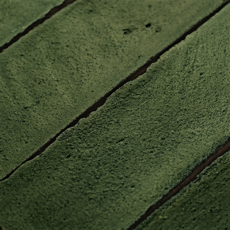 Ladrilhos de terracota verde formam um padrão retangular, organizados em uma grade, criando uma superfície rústica e texturizada