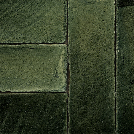 Les carreaux de terre cuite verte forment un motif rectangulaire, soigneusement disposés en grille, créant une surface texturée 