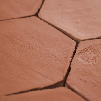 Les carreaux hexagonaux en terre cuite forment un sol rustique, affichant des fissures naturelles et des tons terreux selon un m