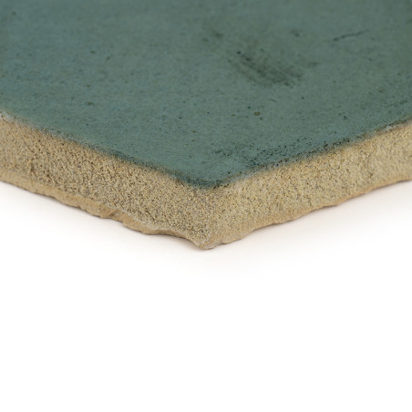 Terracotta tegel met een ruwe beige onderkant, voorzien van een glad groen geglazuurd oppervlak, liggend op een witte achtergron